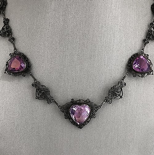 A turn of the centurynecklace featuring an 18ct rose-cut amethyst in a heart shape, surrounded by intricate vintage detailing, set in 18K yellow gold
